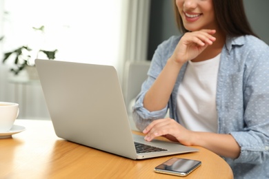 Photo of Young woman using laptop for search at wooden table in room, closeup