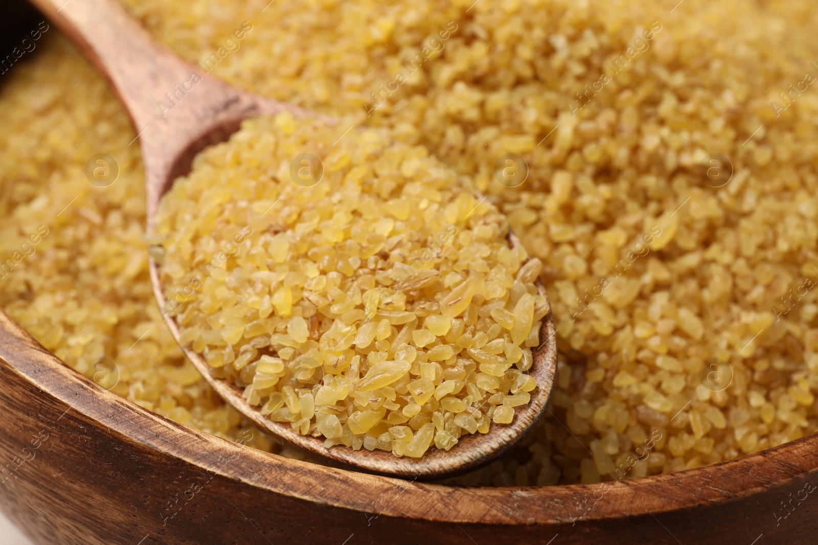 Photo of Wooden bowl and spoon with raw bulgur, closeup