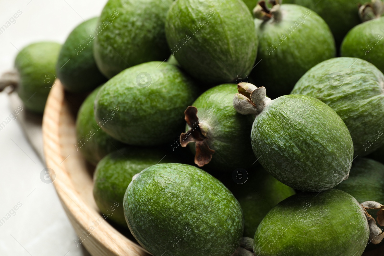 Photo of Fresh green feijoa fruits in bowl on light table, closeup