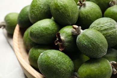 Fresh green feijoa fruits in bowl on light table, closeup