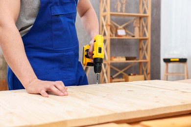 Young worker using electric drill at table in workshop, closeup