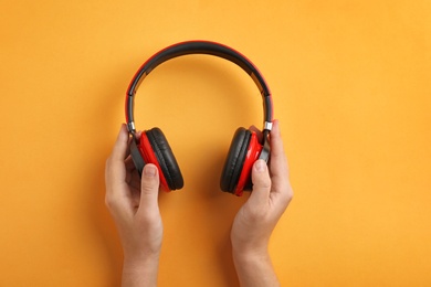 Woman holding headphones on color background, top view