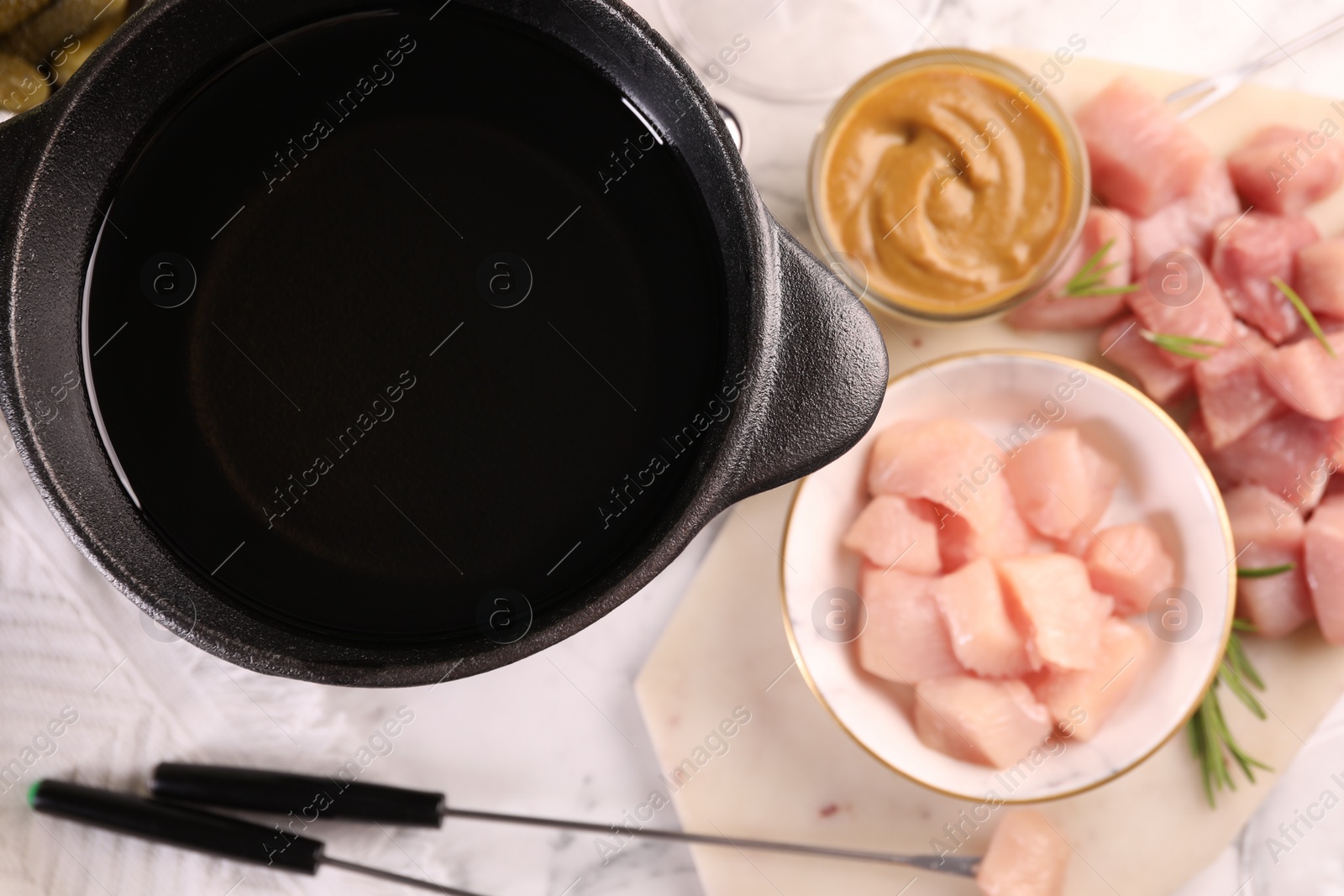 Photo of Fondue pot with oil, forks and raw meat pieces on white marble table, flat lay