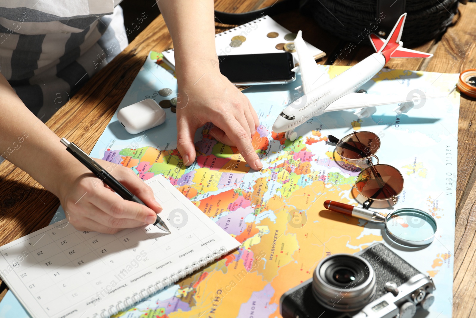 Photo of Woman marking calendar at table with world map, closeup. Travel during summer vacation