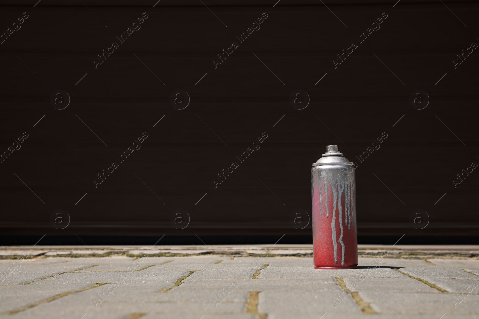 Photo of Used can of spray paint on pavement near black wall outdoors, space for text. Graffiti supplies