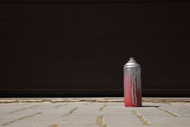 Photo of Used can of spray paint on pavement near black wall outdoors, space for text. Graffiti supplies