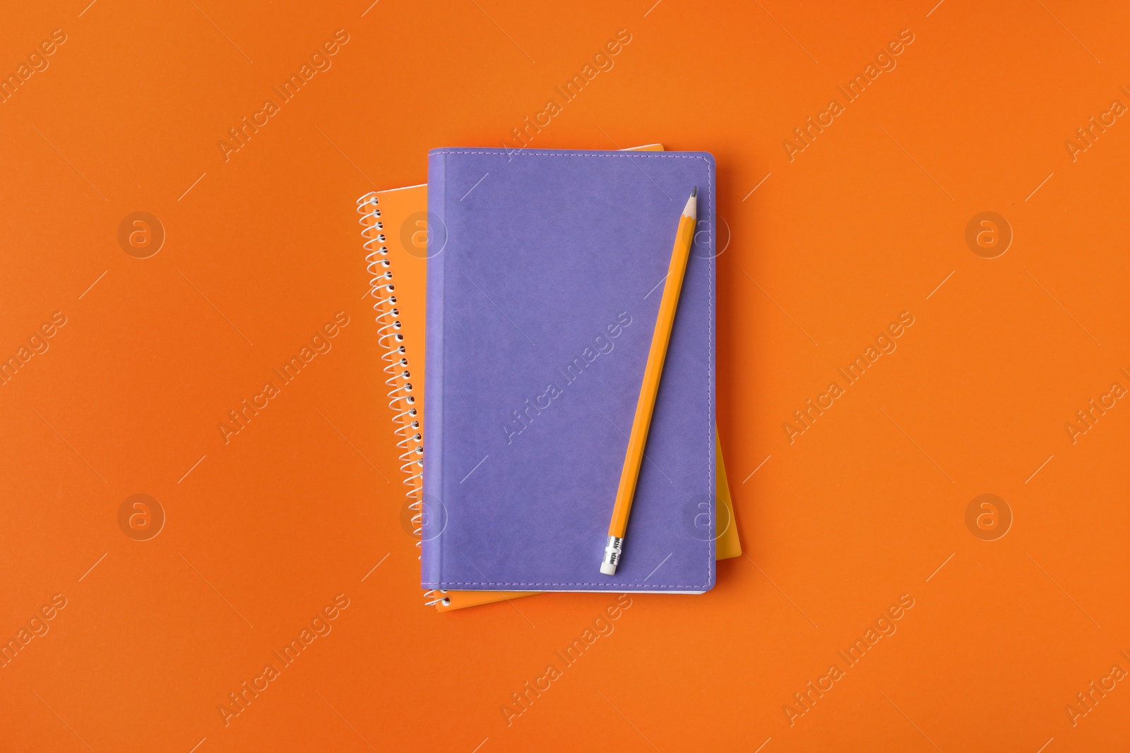 Photo of Notebooks with pencil on orange background, top view