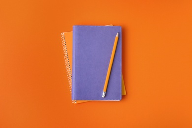 Photo of Notebooks with pencil on orange background, top view