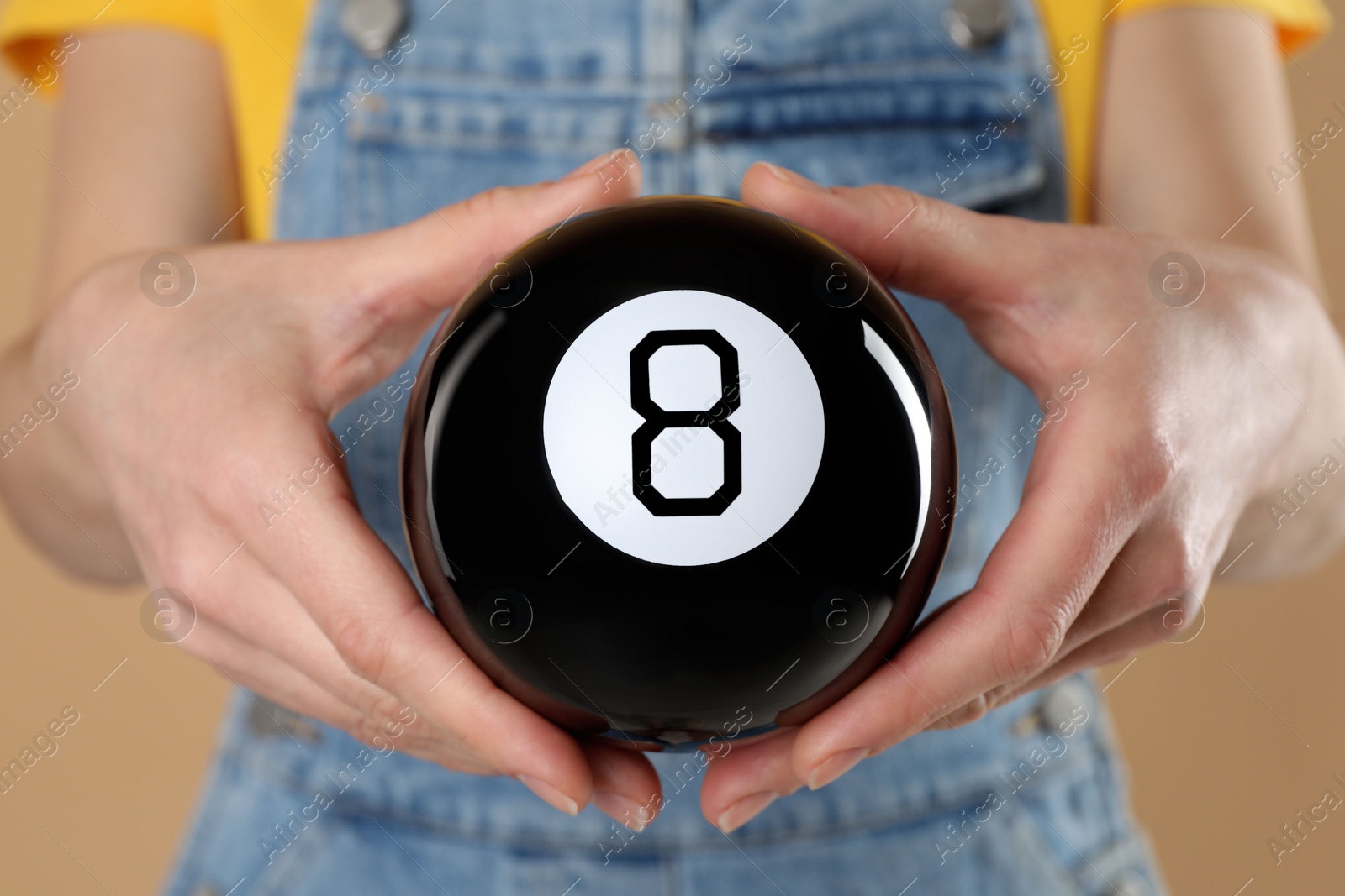 Photo of Woman holding magic eight ball on light brown background, closeup