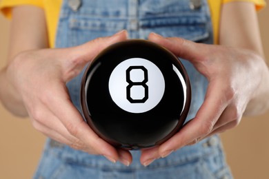 Photo of Woman holding magic eight ball on light brown background, closeup