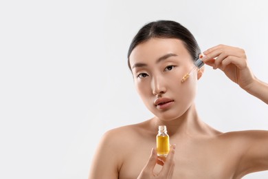Photo of Beautiful young woman applying cosmetic serum onto her face on white background, space for text