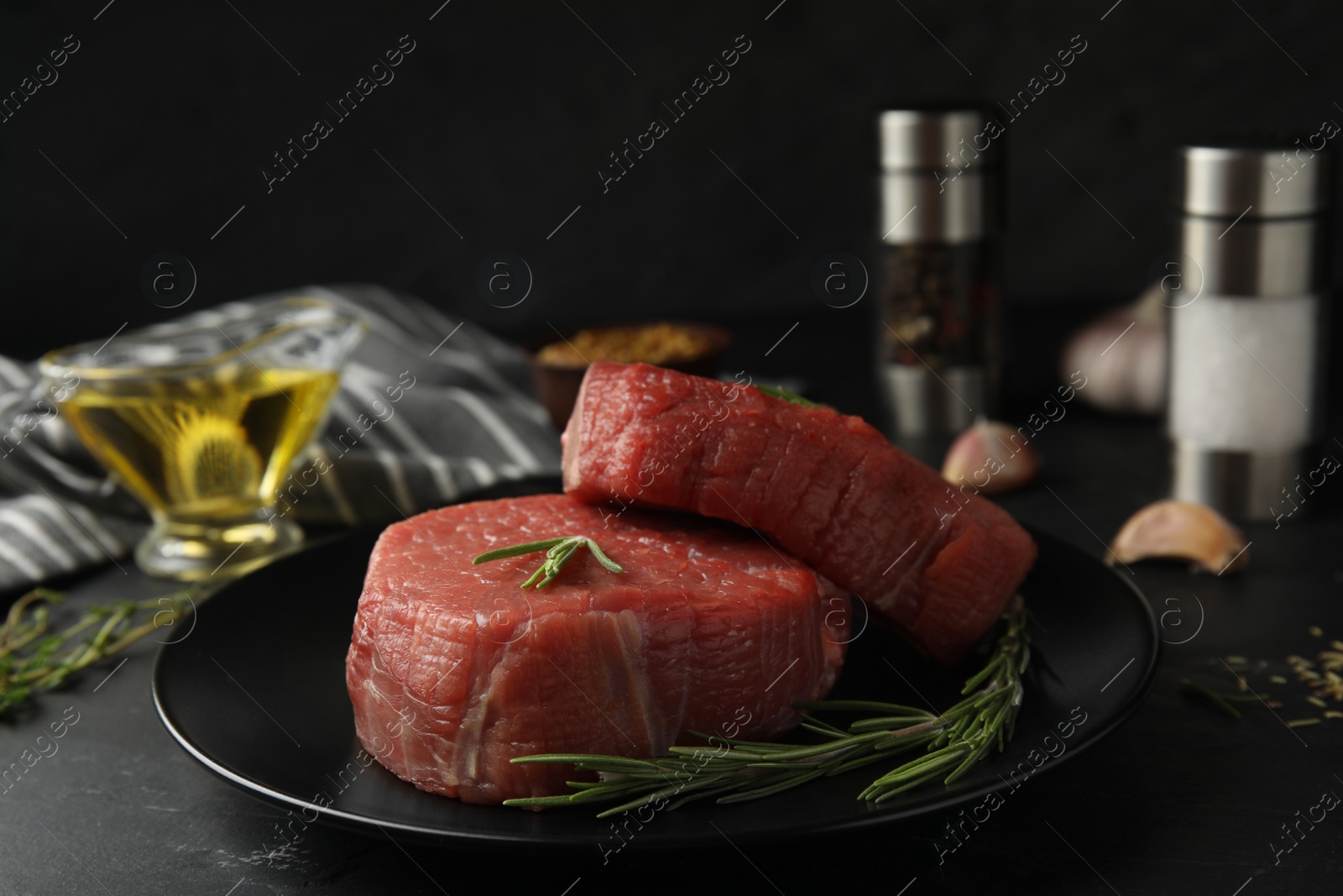 Photo of Fresh raw beef cut with rosemary on black table, closeup