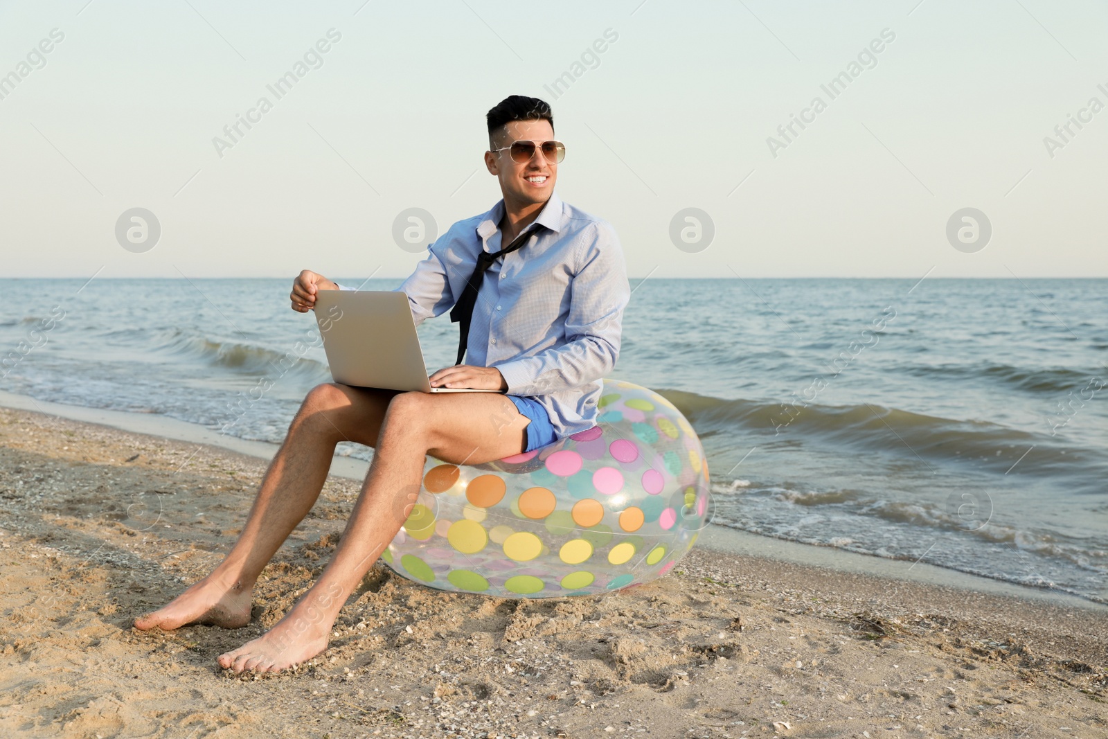 Photo of Happy businessman working with laptop on beach. Business trip