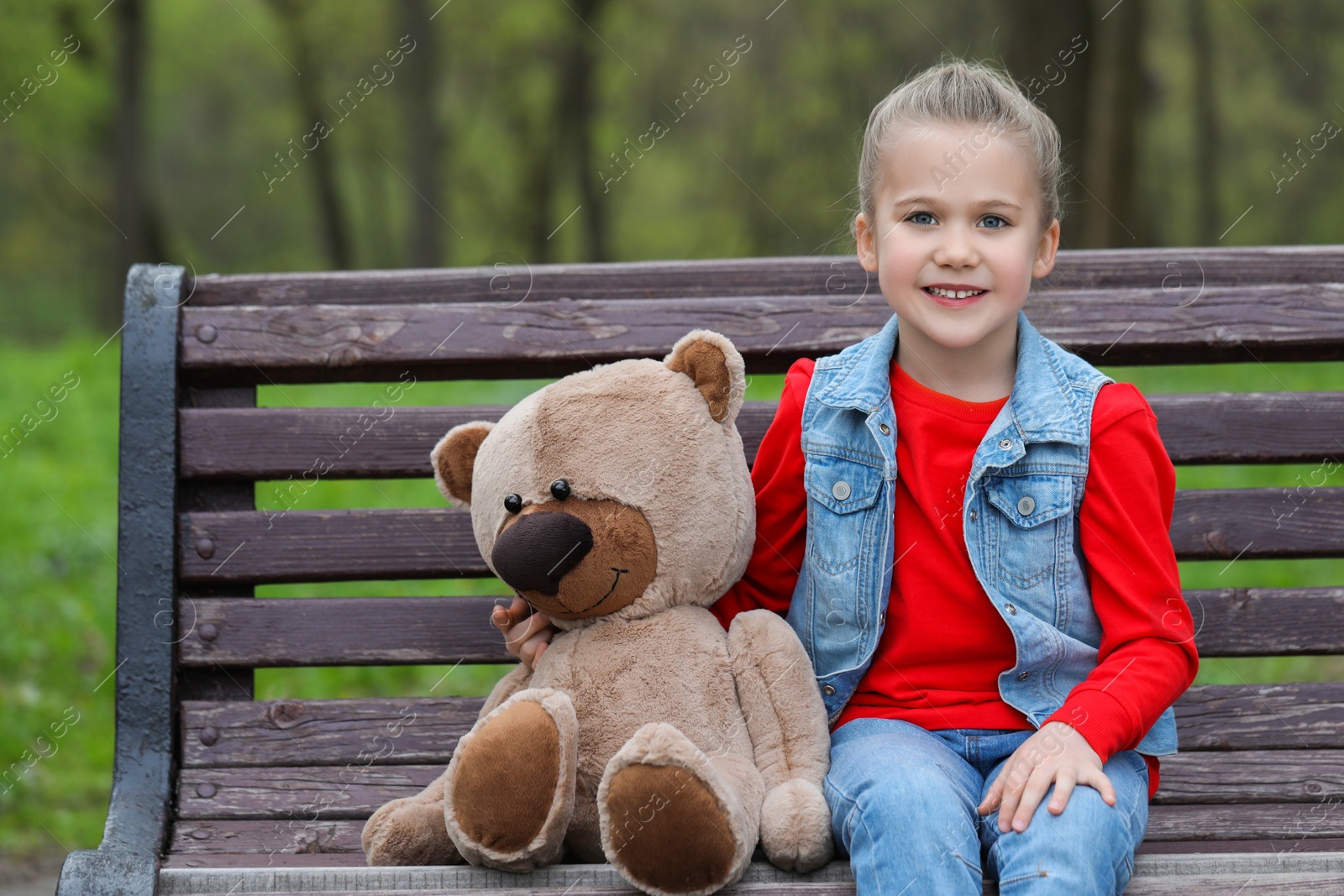 Photo of Little girl with teddy bear on wooden bench outdoors. Space for text