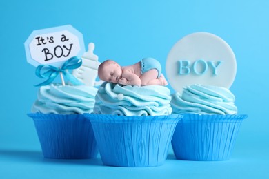 Photo of Beautifully decorated baby shower cupcakes for boy with cream and toppers on light blue background