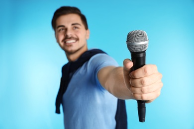 Photo of Young handsome man in casual clothes holding microphone on color background