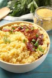 Photo of Tasty millet porridge with bacon, green onion and dill in bowl on light blue wooden table, closeup