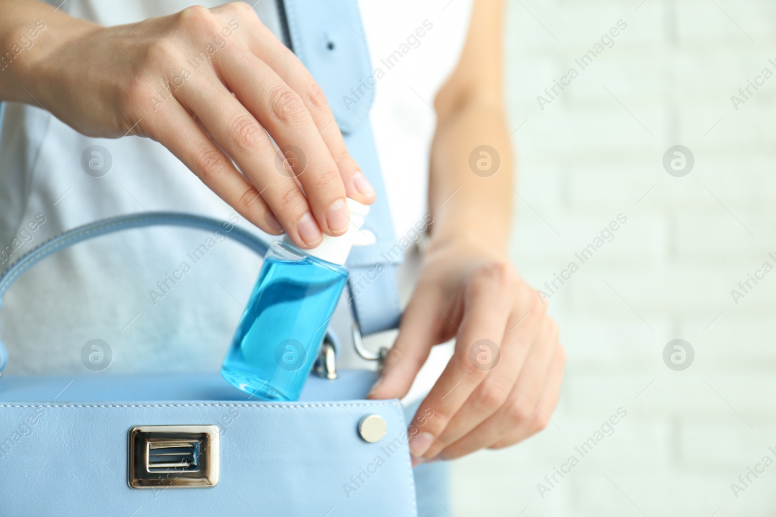 Photo of Woman putting hand sanitizer in purse on light background, closeup. Personal hygiene during COVID-19 pandemic