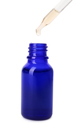 Essential oil dripping from pipette into glass bottle on white background