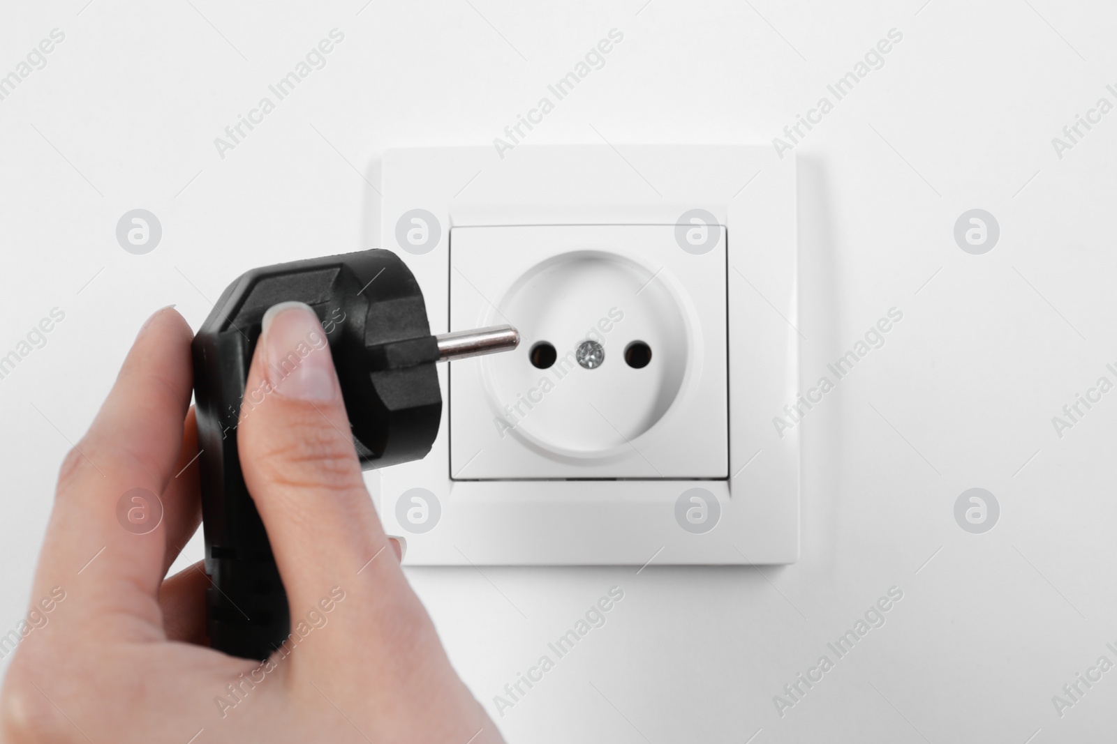 Photo of Woman putting plug into power socket on white background, closeup. Electrician's equipment