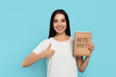 Happy woman holding notebook with words Keto Diet on turquoise background