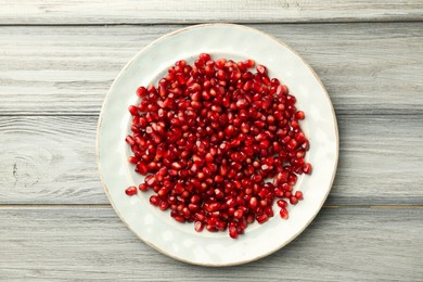 Photo of Tasty ripe pomegranate grains on light wooden table, top view