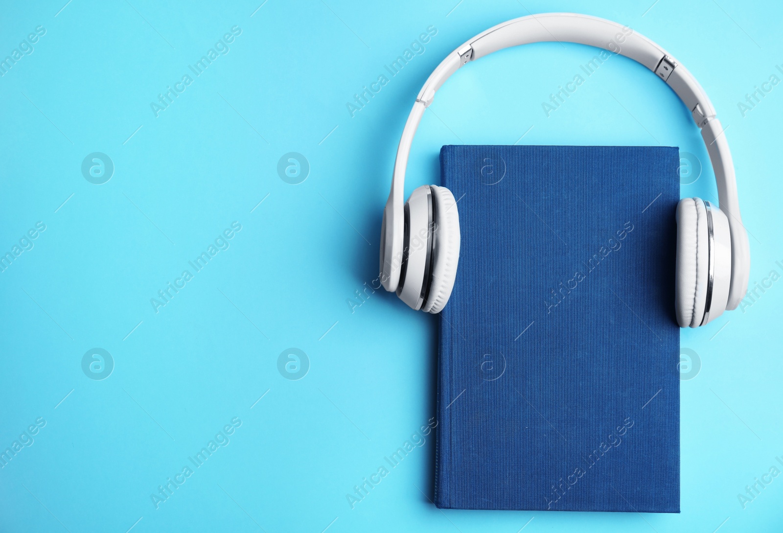 Photo of Book and modern headphones on light blue background, top view. Space for text
