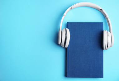 Book and modern headphones on light blue background, top view. Space for text