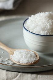 Photo of Organic salt in bowl and wooden spoon on table, closeup