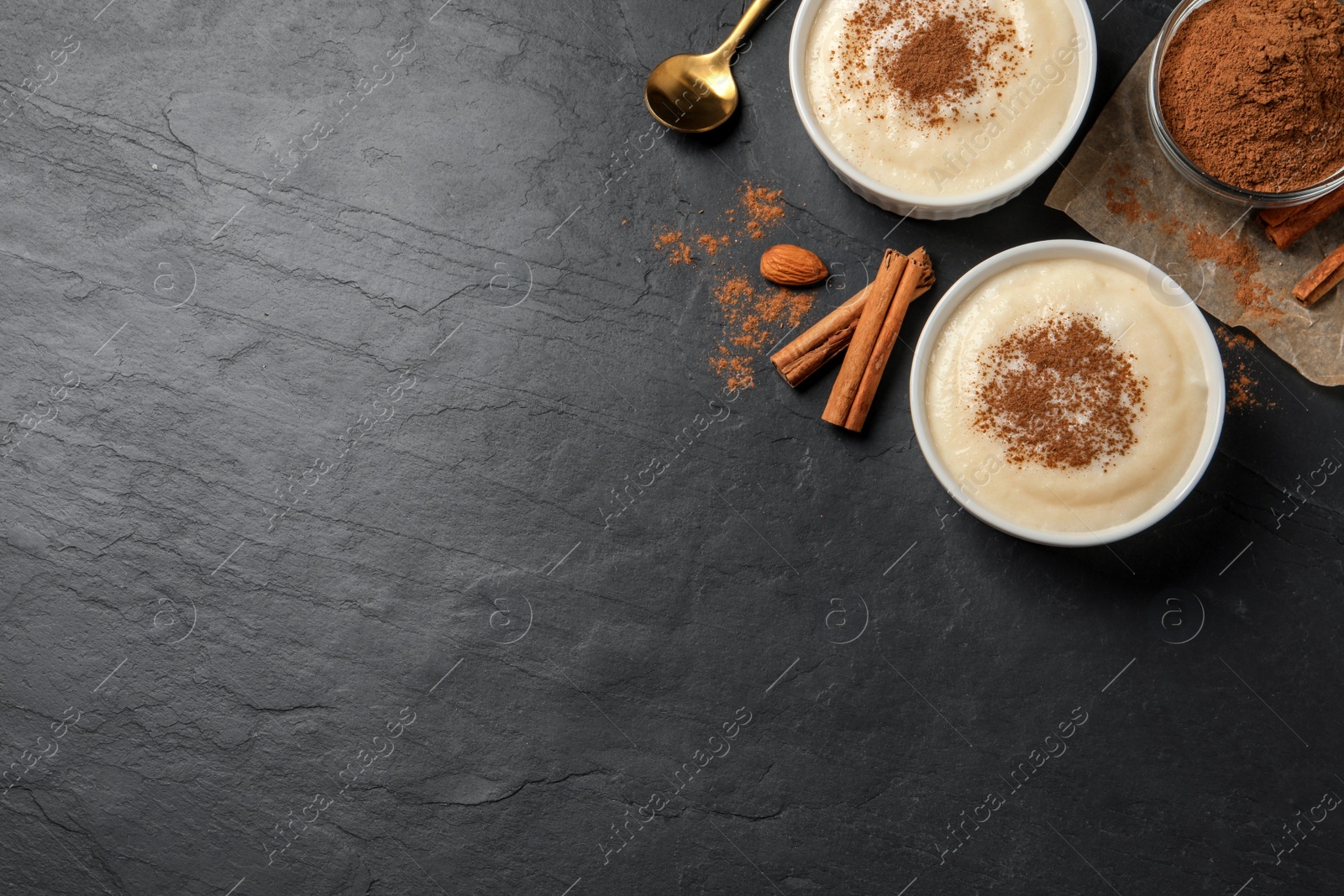 Photo of Delicious semolina pudding with cinnamon on black table, flat lay. Space for text