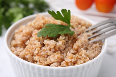 Tasty wheat porridge with parsley in bowl on table, closeup