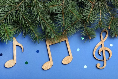 Fir tree branches with wooden music notes on blue background, flat lay. Christmas celebration