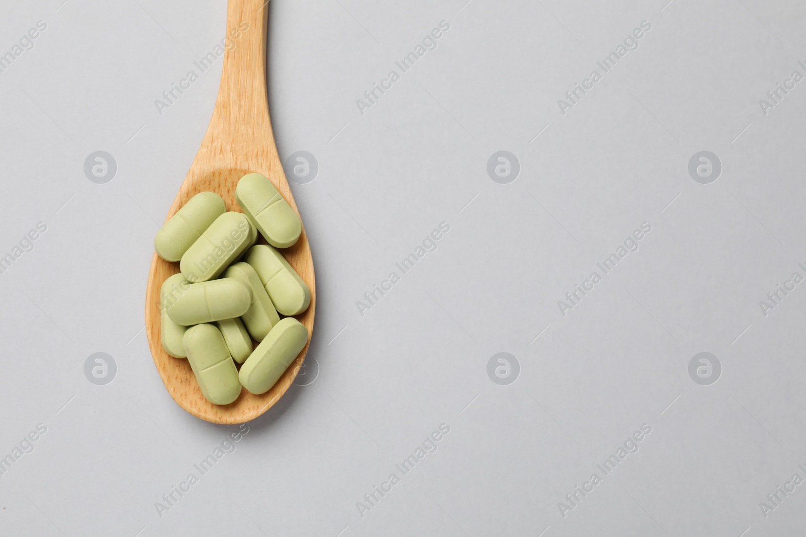 Photo of Vitamin capsules in wooden spoon on light grey background, top view. Space for text