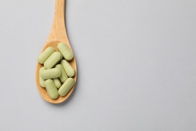 Photo of Vitamin capsules in wooden spoon on light grey background, top view. Space for text