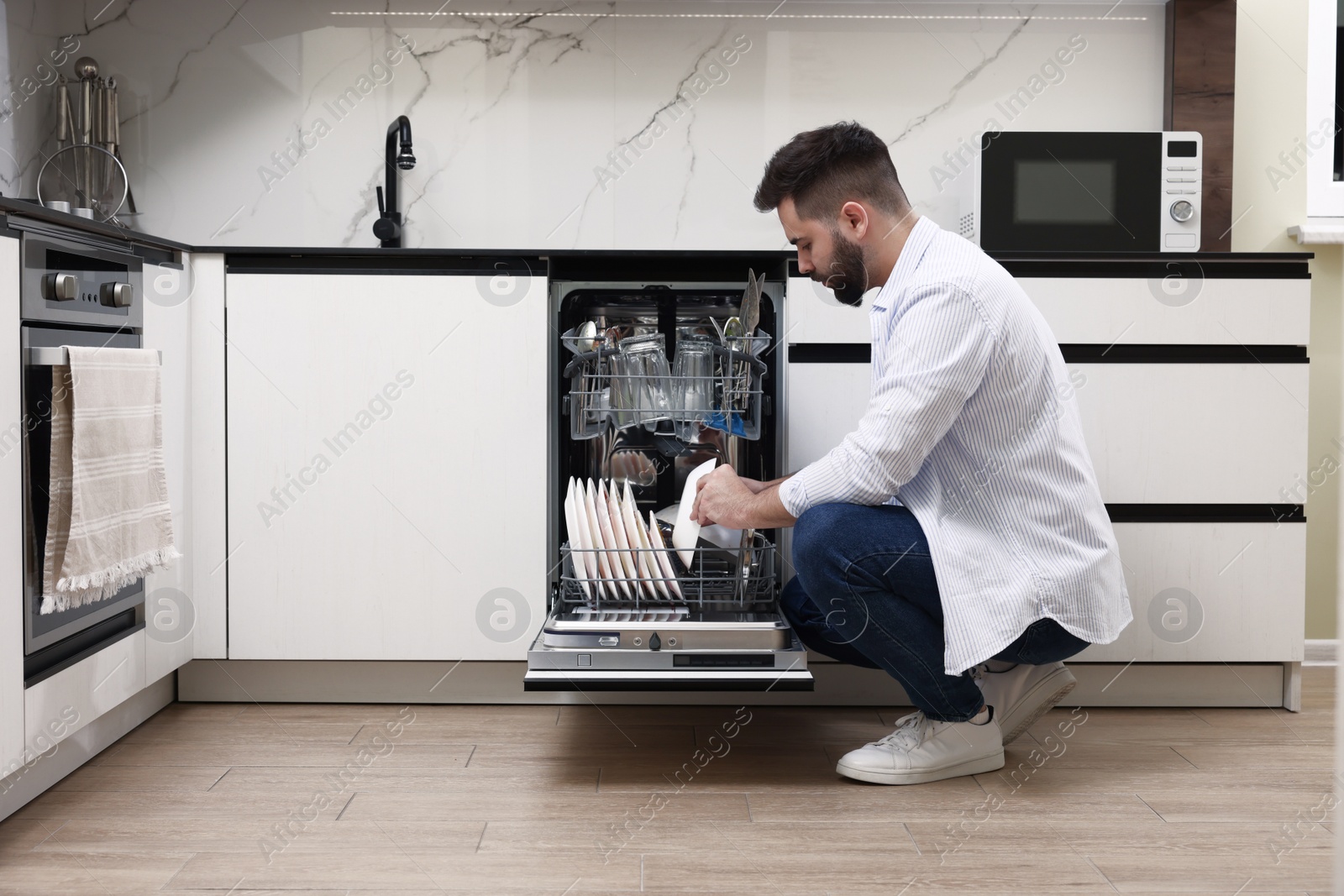 Photo of Man loading dishwasher with dirty plates indoors