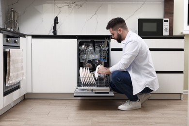 Man loading dishwasher with dirty plates indoors