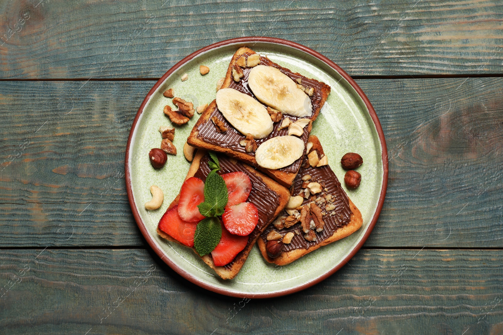 Photo of Tasty toasts with chocolate spread, nuts, strawberries, banana and mint served on wooden table, top view