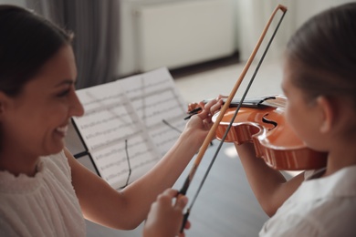 Photo of Young woman teaching little girl to play violin indoors, focus on hands