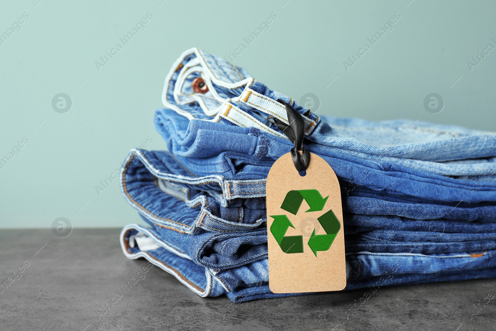 Image of Stack of jeans with recycling label on grey table 