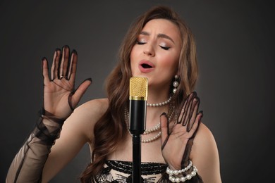 Beautiful young woman with microphone singing on dark background