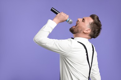 Handsome man with microphone singing on violet background. Space for text