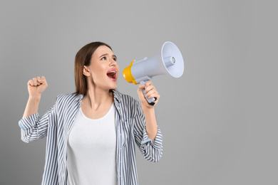 Photo of Emotional young woman with megaphone on light grey background. Space for text
