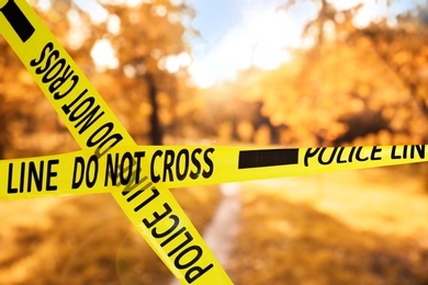 Yellow police tape isolating crime scene. Blurred view of autumn park 