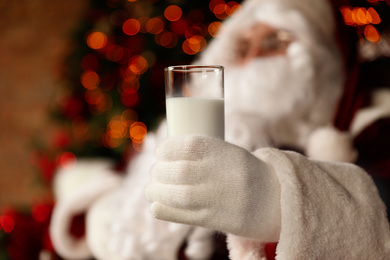 Photo of Santa Claus holding glass of milk against blurred Christmas lights, closeup