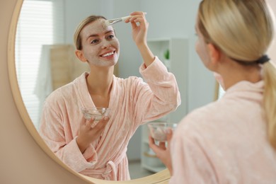 Photo of Woman applying face mask near mirror in bathroom. Spa treatments