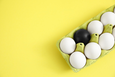 Black egg among others in box on yellow background, top view. Space for text