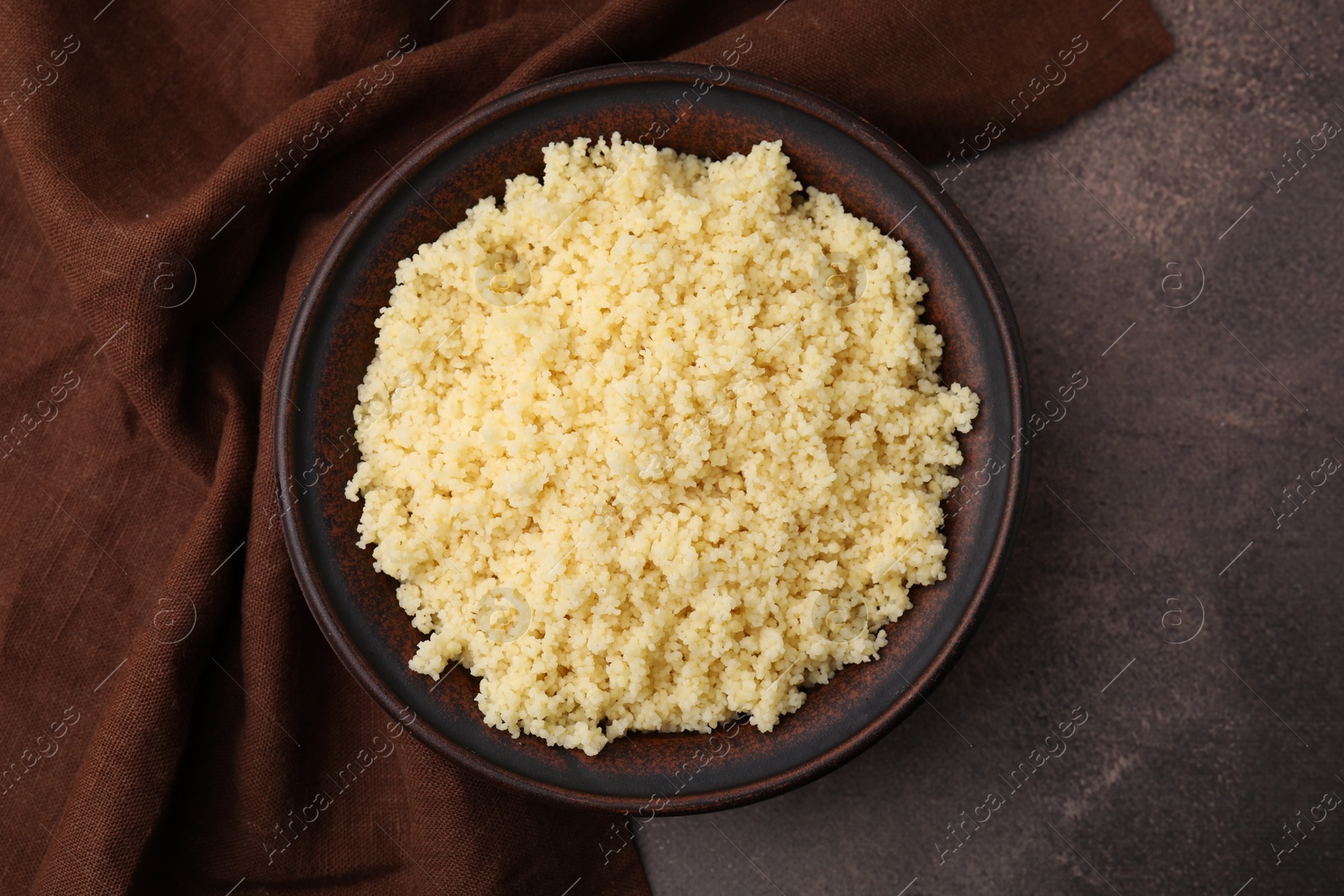 Photo of Tasty couscous in bowl on brown table, top view
