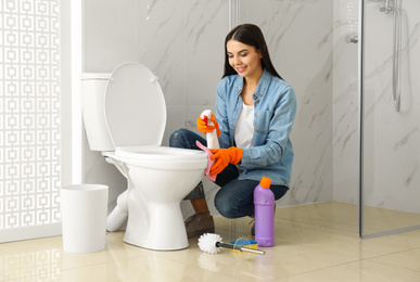 Young woman cleaning toilet bowl in bathroom