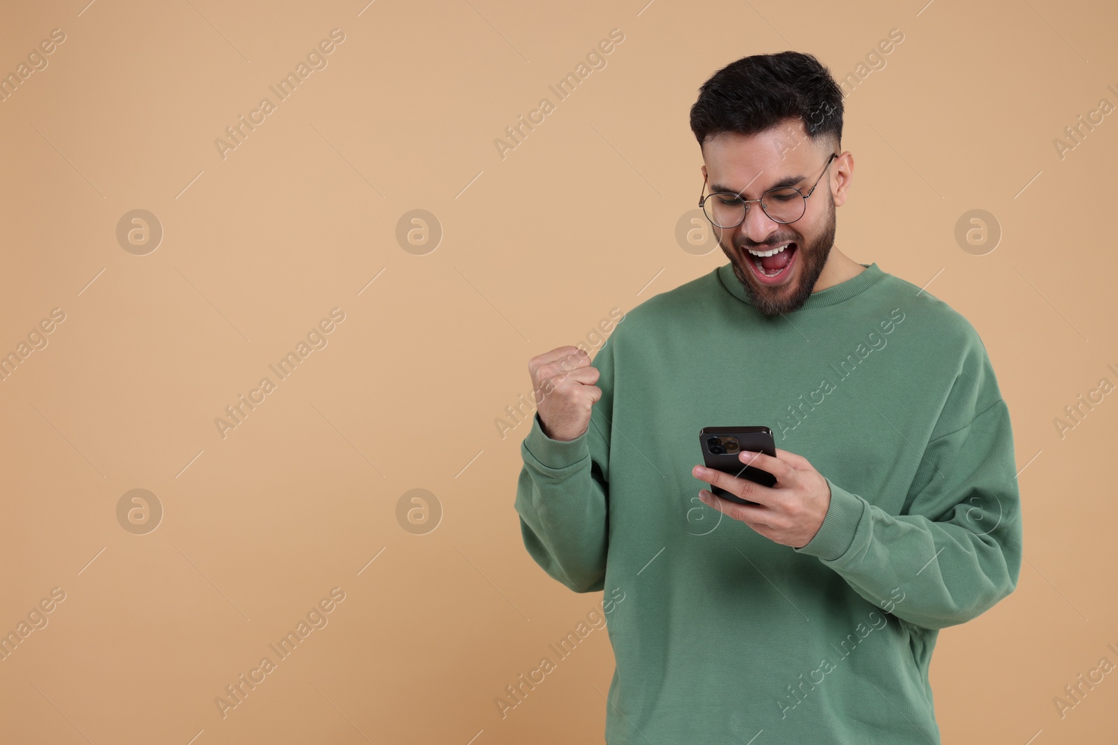 Photo of Happy young man using smartphone on beige background, space for text