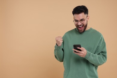 Happy young man using smartphone on beige background, space for text